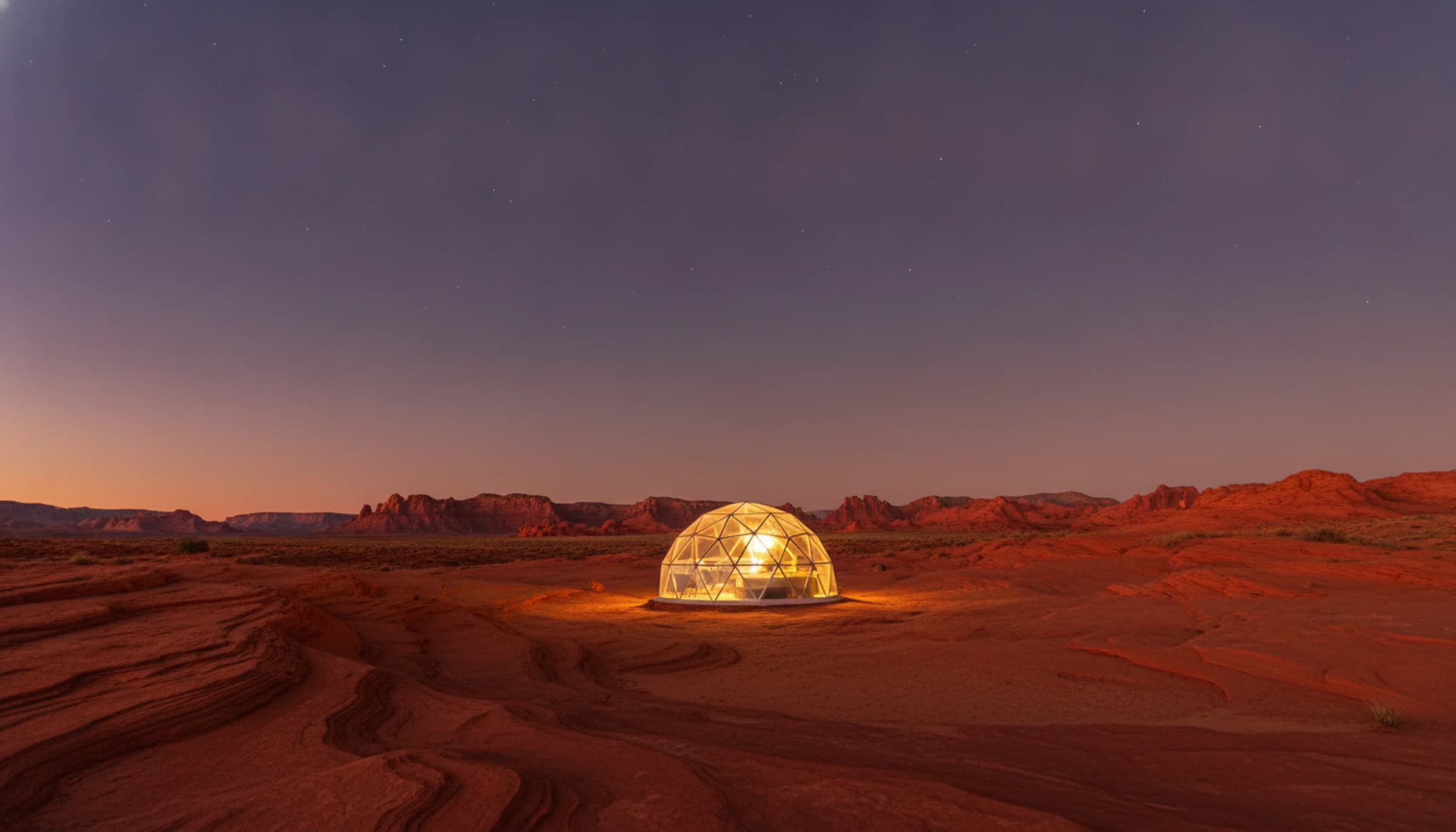 A lit geodesic dome on red slickrock under a deep blue-hour sky with the first stars out, near Capitol Reef National Park