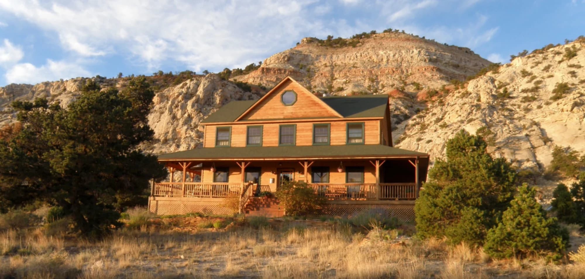 The Lodge — a two-storey timber building with a wraparound covered deck, below sandstone cliffs and pinyon pine near Capitol Reef National Park